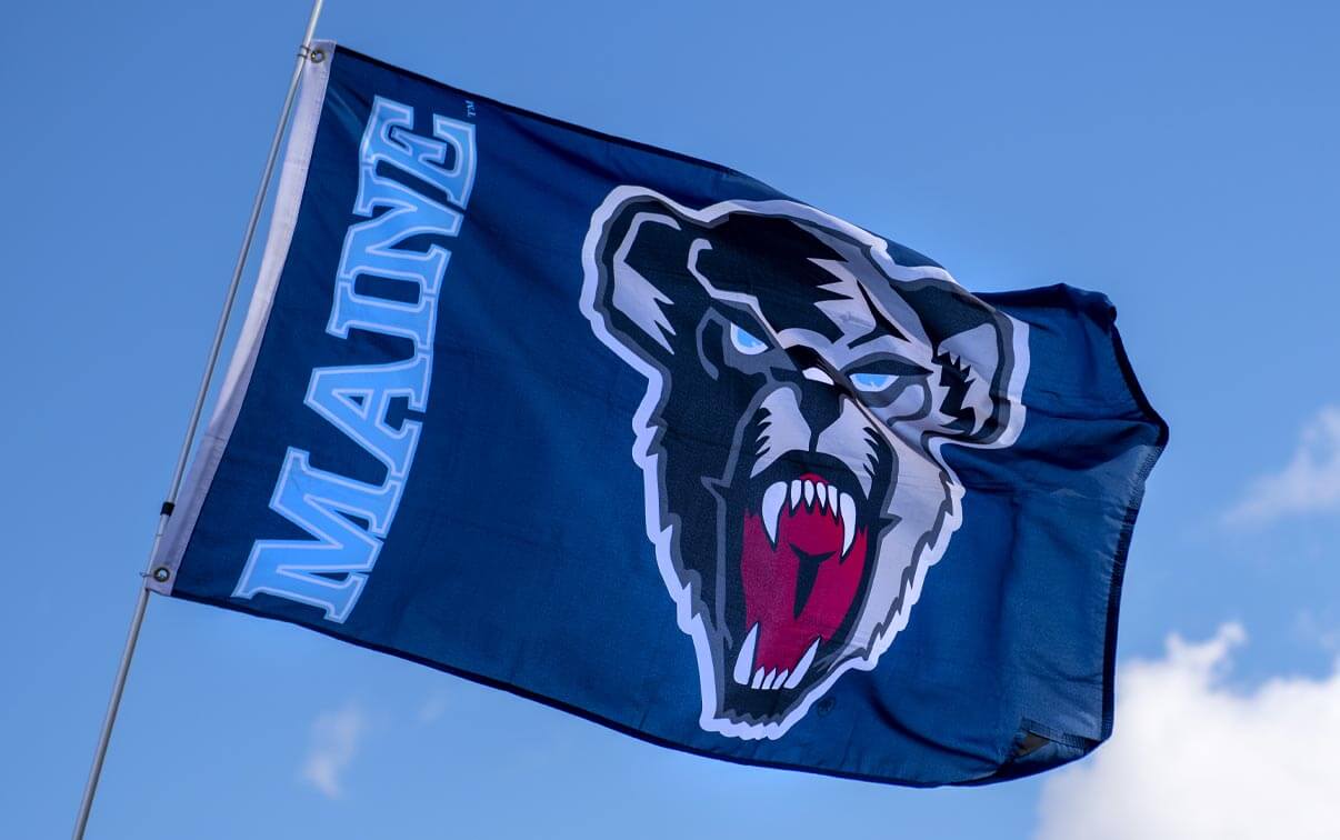 A photo of a UMaine Black Bears flag against a blue sky