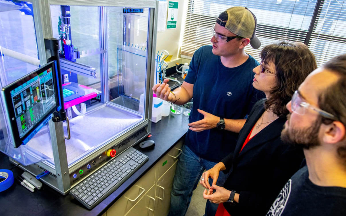 A photo of three people looking at an experiment