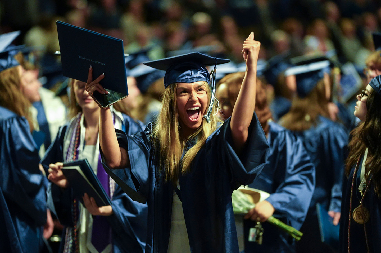UMaine student cheering in a cap and gown at commencement