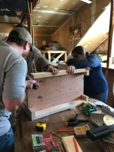 Our team was building the middle portion of the table and adding legs to it. Some members were holding the planks of wood in place, while another screwed the wood together.