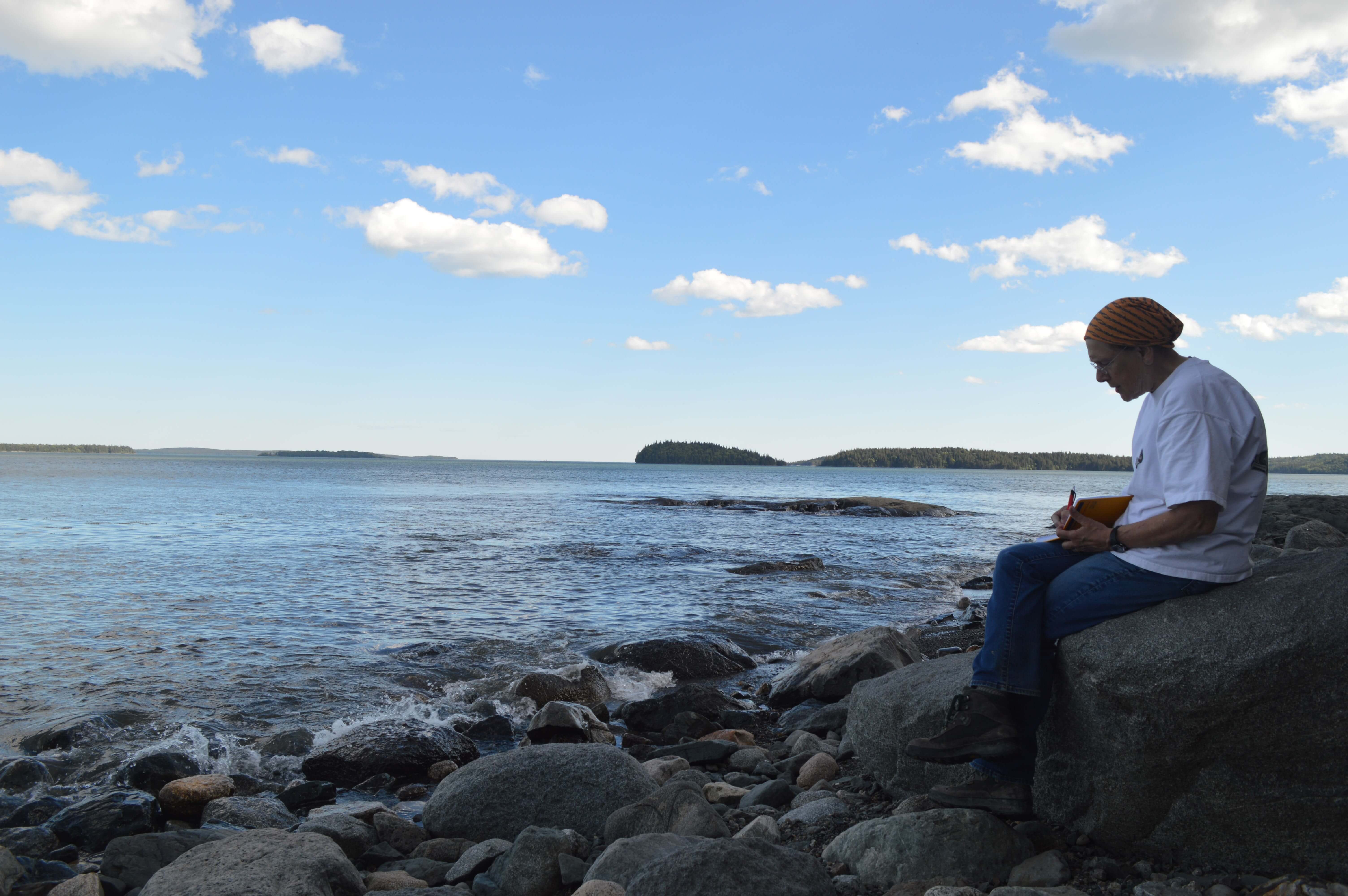 Alice Kelley sitting on a rock writing in her field journal