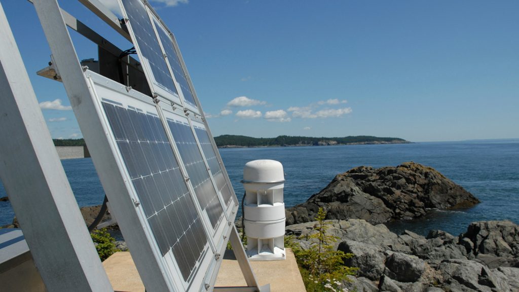 Solar panels on cement platform on rocky outcrop looking out to ocean and island on Maine coast