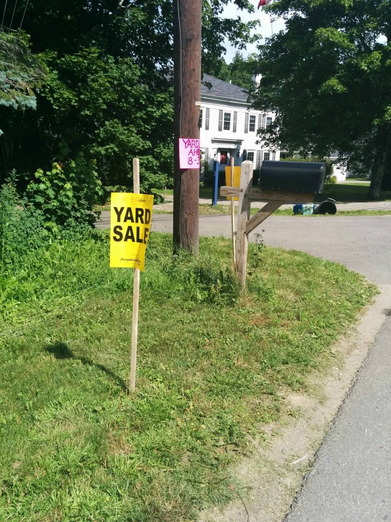 Image of a lawn with a yellow sign that reads "yard sale"