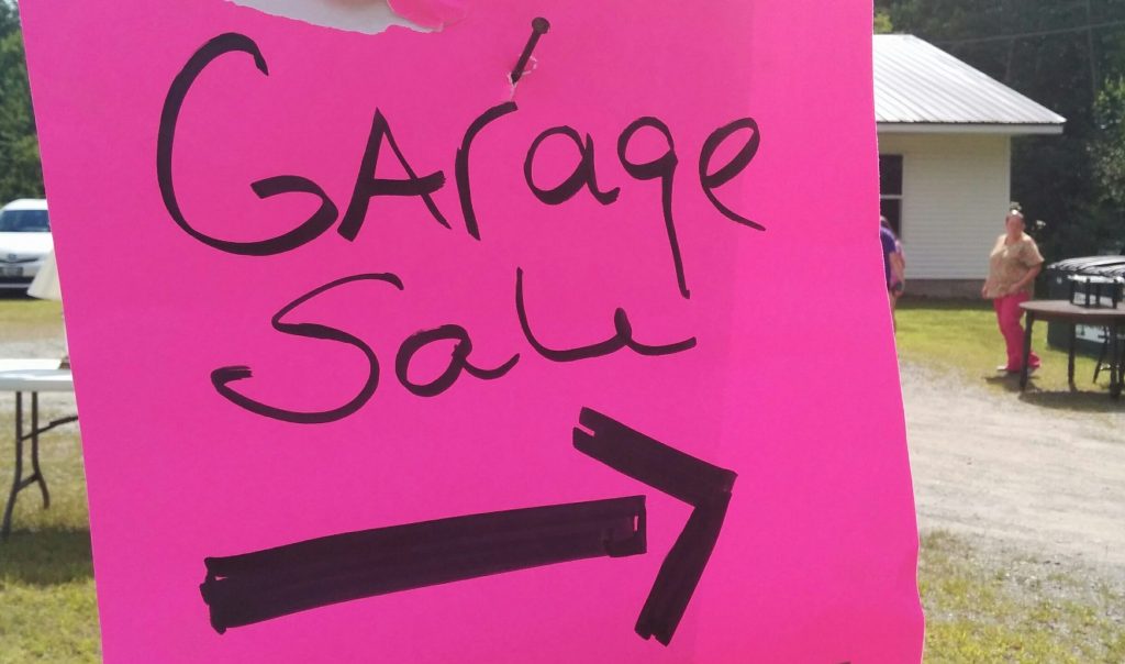 Image of pink homemade sign that reads "Garage Sale" with an arrow