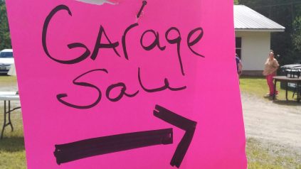 Image of pink homemade sign that reads "Garage Sale" with an arrow