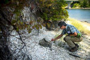 Stephen Claeson kneeling at shell midden along shoreline