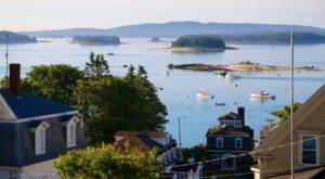 Looking out rooftops on the harbor in Stonington Maine with islands and fishing boats in the distance