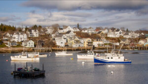 Harbor in Stonington, Maine, looking onshore from the water, with fishing boats in foreground and town behind