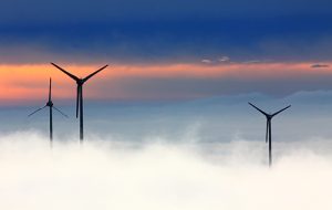 Three windmills rising out of clouds at sunrise