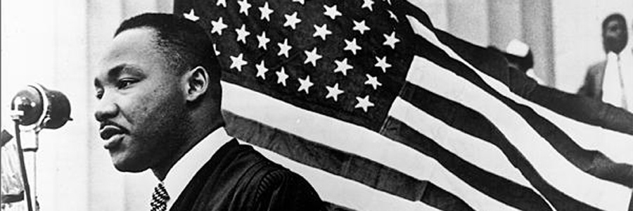 Martin Luther King Jr speaking into microphone in front of US Flag