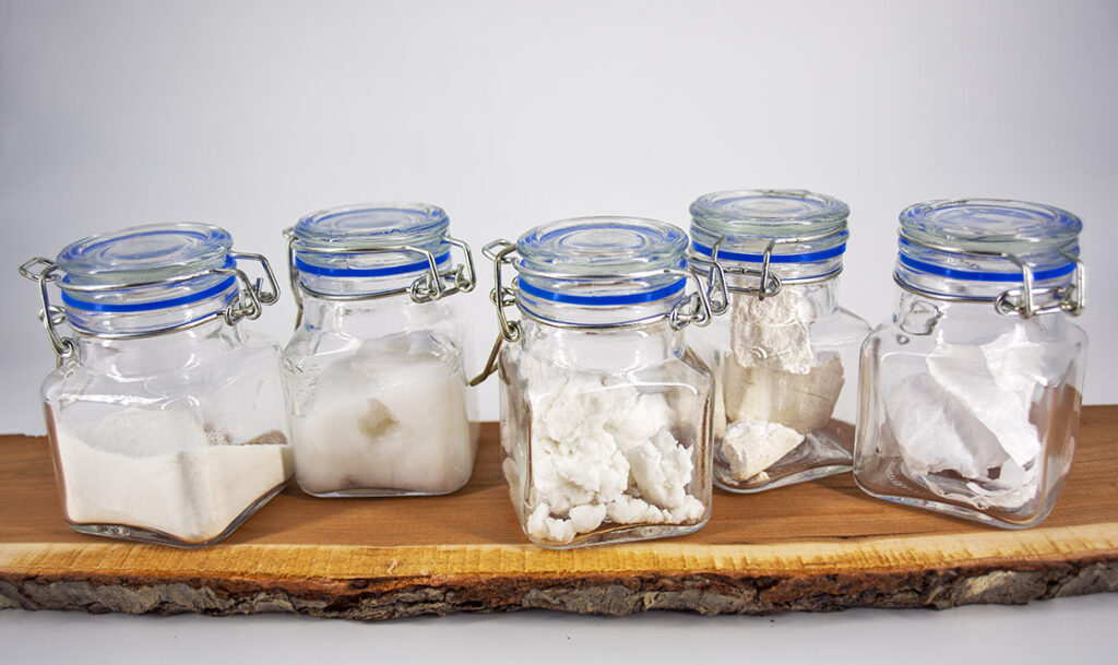 clear jars containing samples of white nanocellulose lined up on a piece of wood