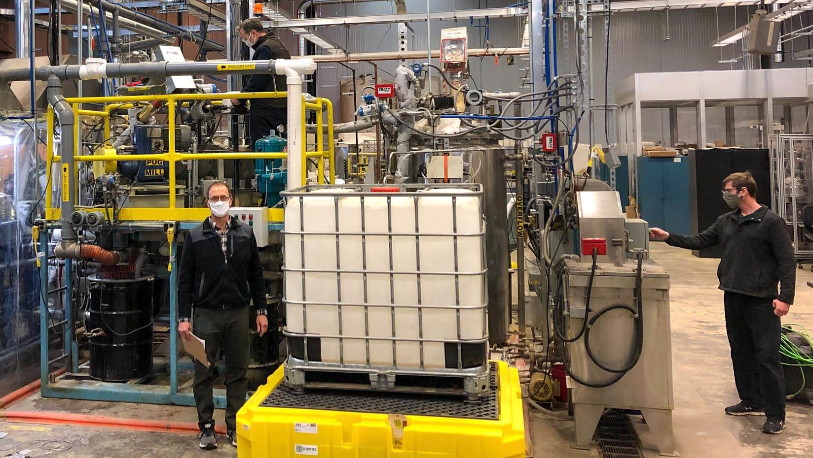 Employees stand in front of large processing equipment