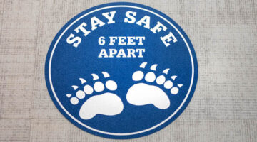 A floor sticker that says stay safe 6 feet apart