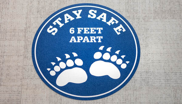 A floor sticker that says stay safe 6 feet apart
