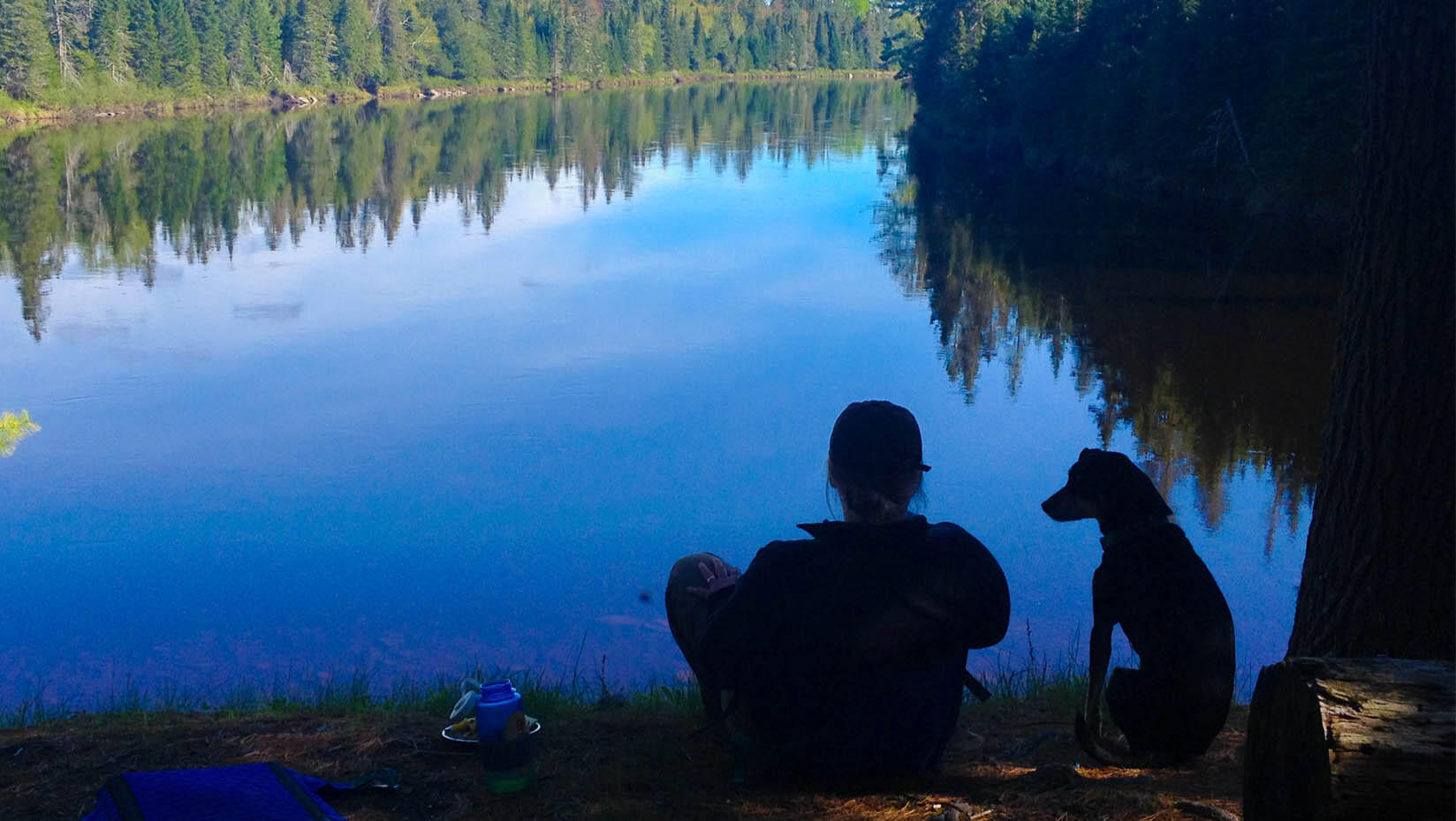 Michelle Moschkau sits on the edge of a lake with a dog