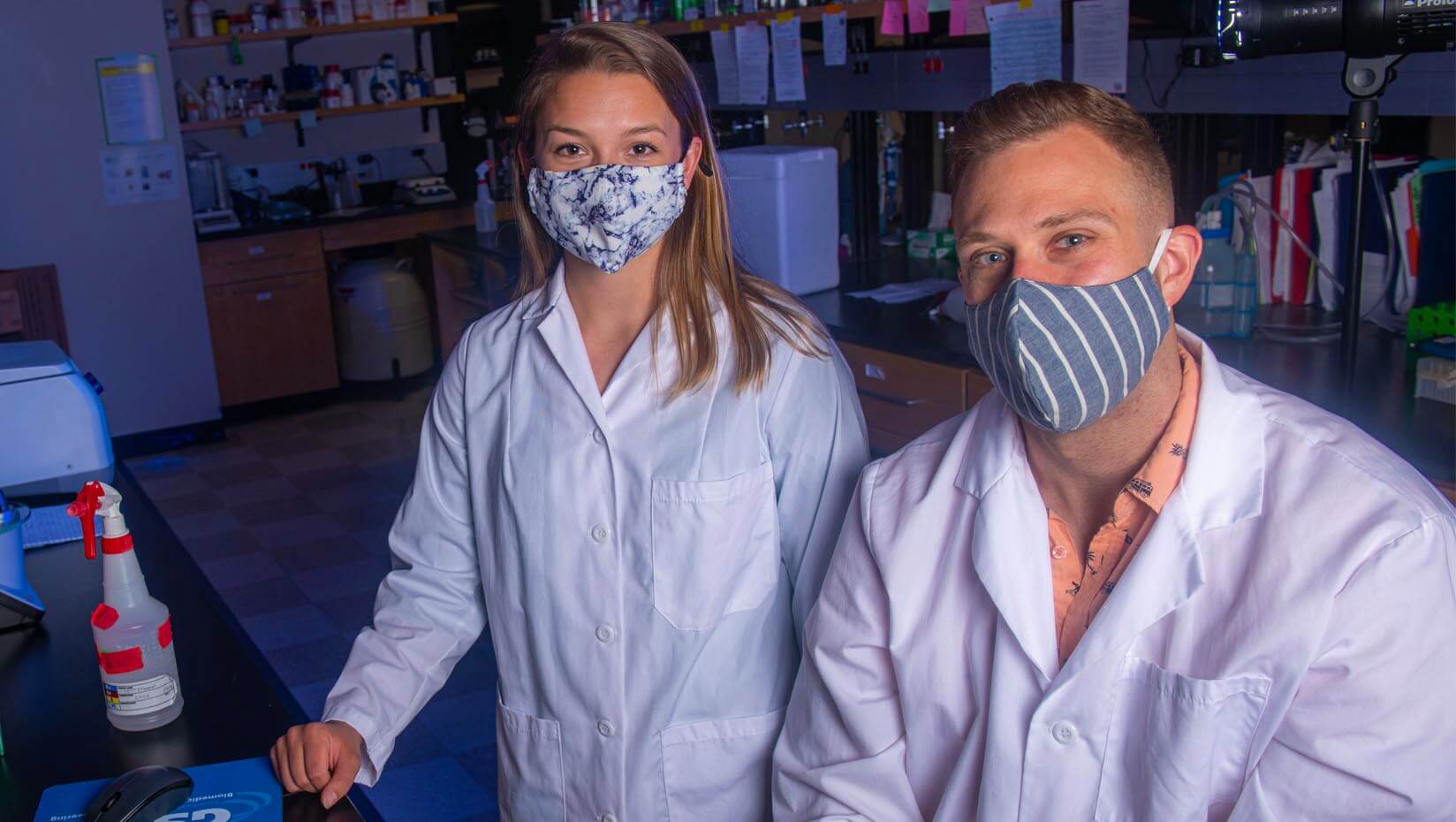 Two students wearing face coverings stand in a lab