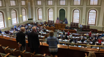 President Ferrini-Mundy, professor George Jacobson, and Maine Chamber of Commerce President Dana Connors standing in balcony of state house while Maine Legislature congratulates UMaine's attainment of R1 research classification