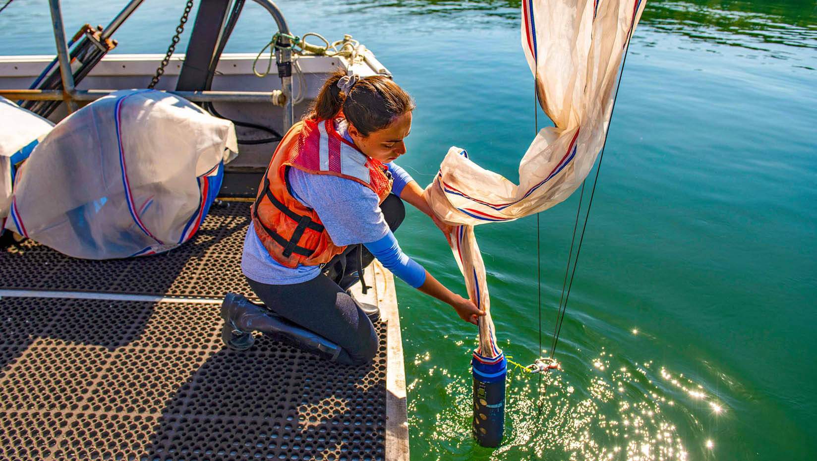 Photo of a student on a research vessel collecting samples of plankton from the water.