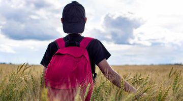 A photo of a person standing in a field wearing a red backpack