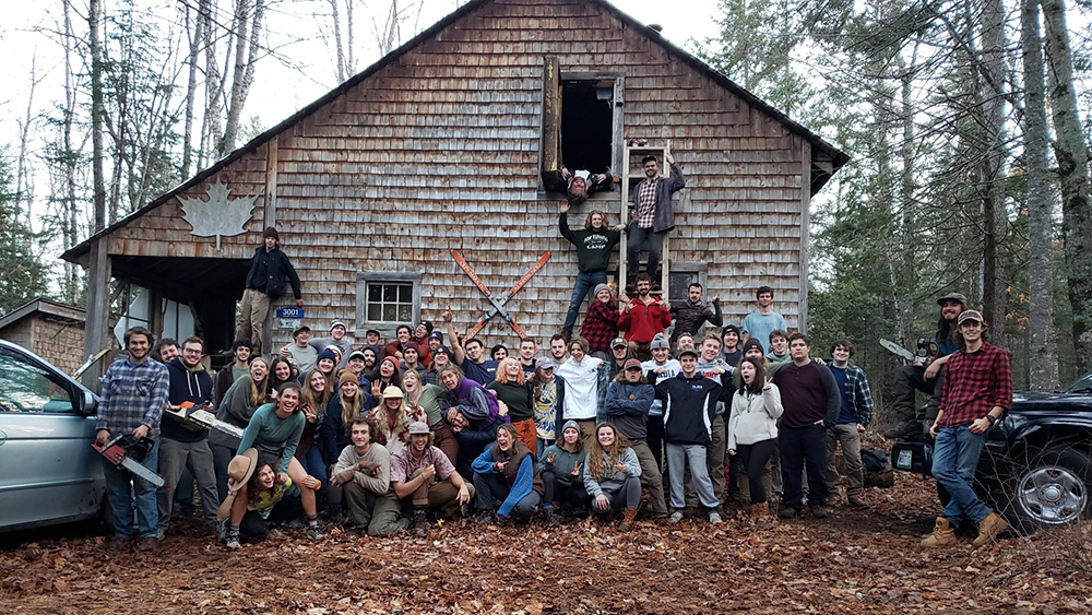 An image of the Maine Outing Club's cabin, with members of the club assembled in front for this group photo