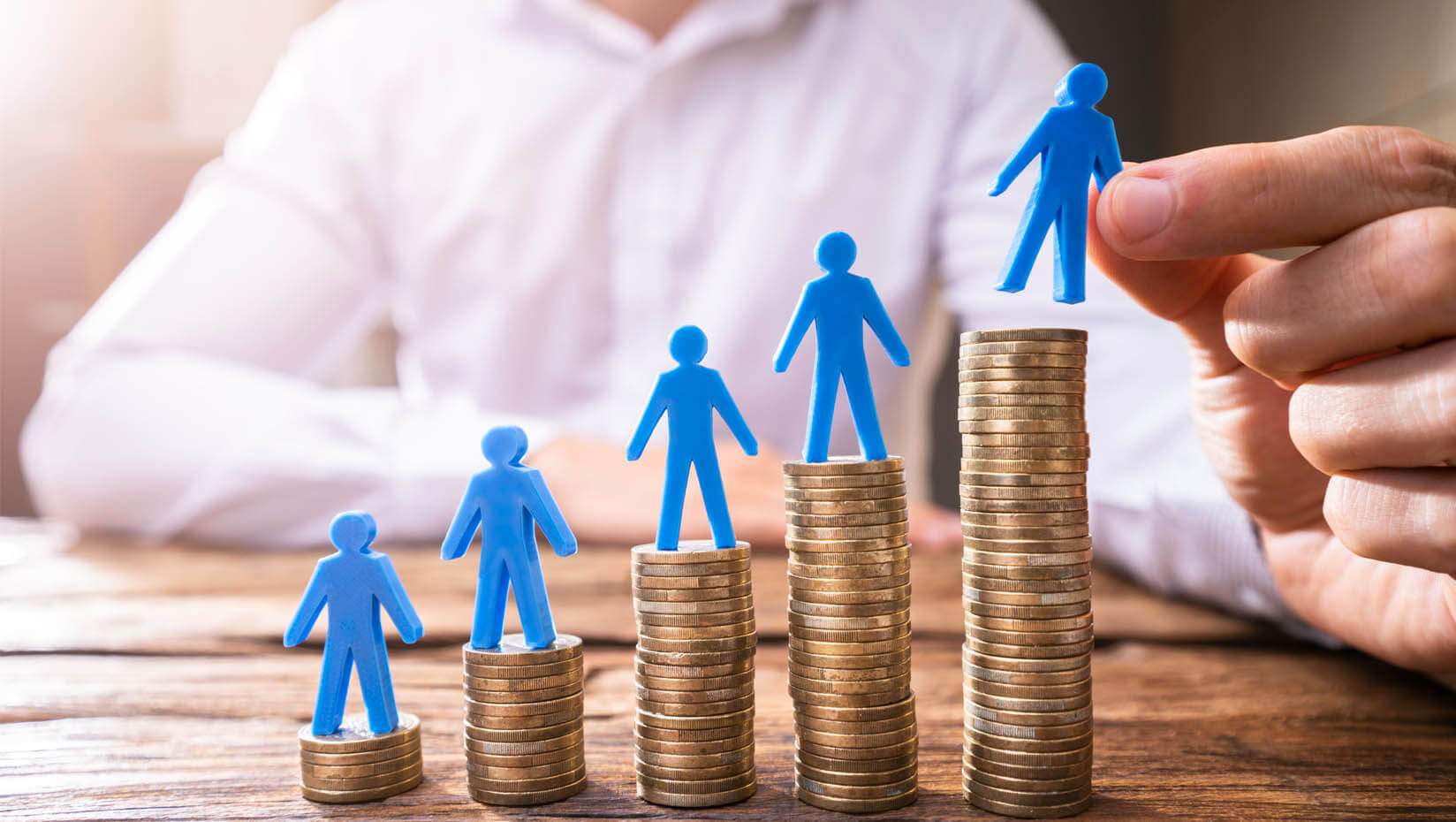 A photo of several stacks of coins increasing in height, topped by little blue figures