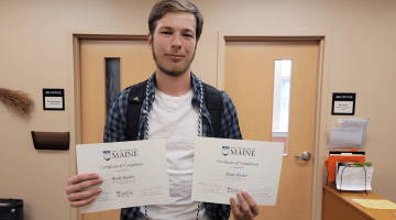 Brady Barker stands holding two UMaine Early College completion certificates