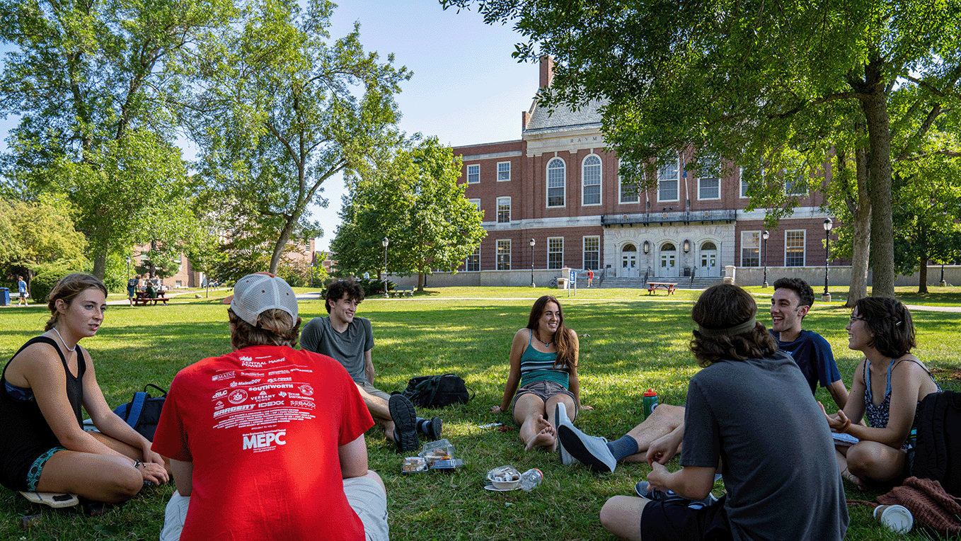 Photo of students sitting in a circle outside on the University of Maine campus