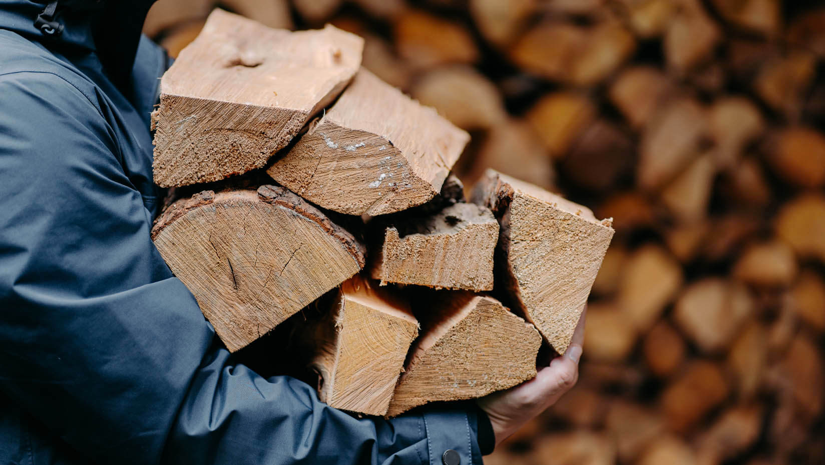 A photo of a person in a winter coat carrying split wood