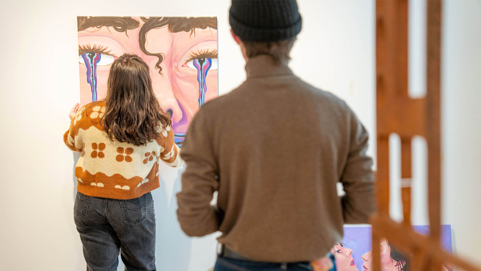 A photo of two people standing in front of a piece of art hanging on a wall