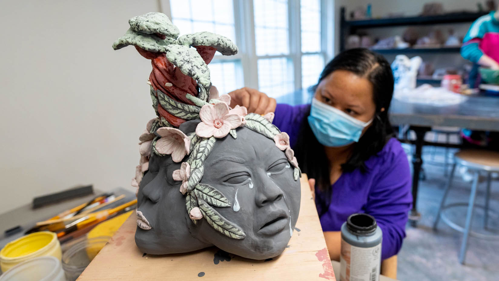 A photo of a masked student working on a ceramics project