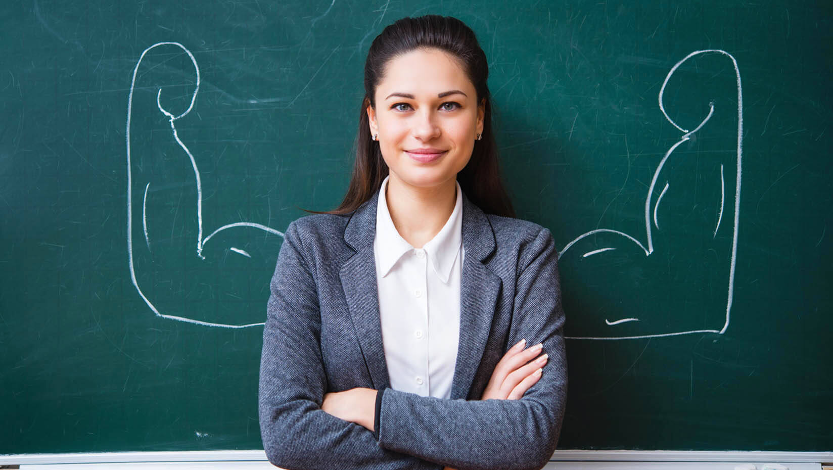 A photo of a teacher standing in front of flexing arms drawn on a chalk board