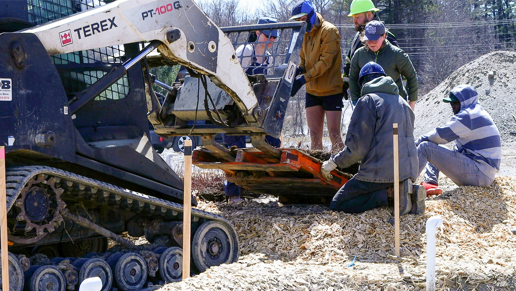 A group of people in hard hats watching a machine add a pallet of wild blueberries to the ground.