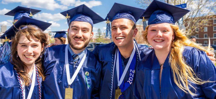 A photo of four graduates smiling at the camera