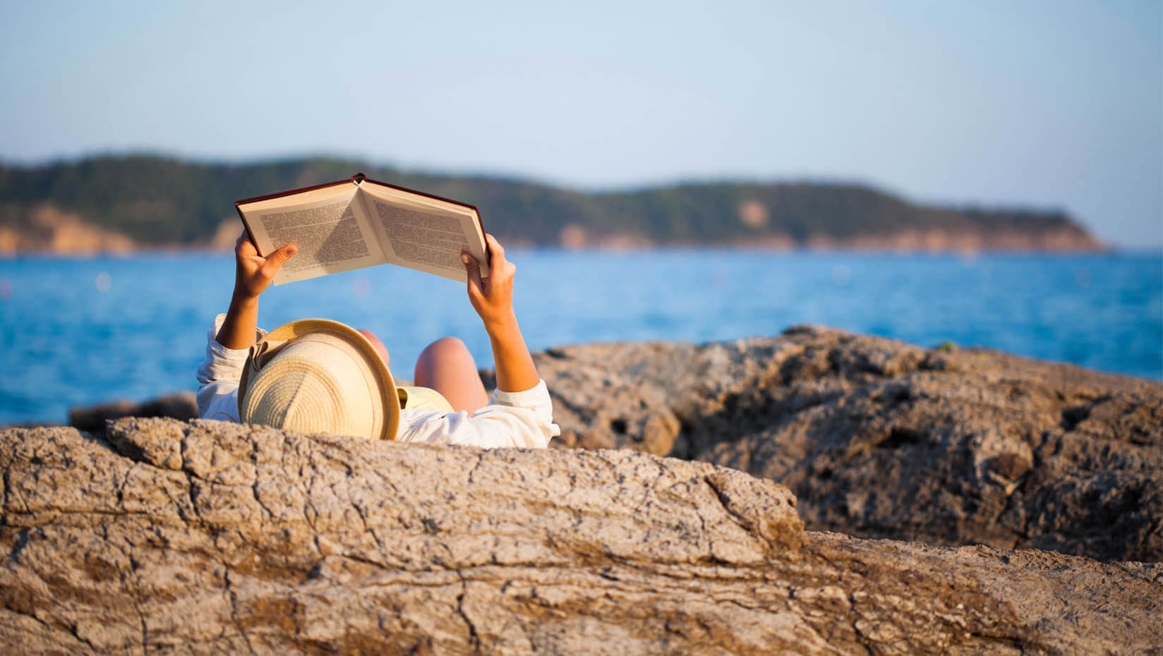 A photo of a person reading on the coast of Maine