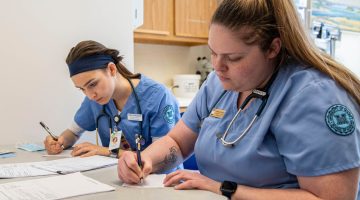 A photo of two nursing students completing paperwork at a table
