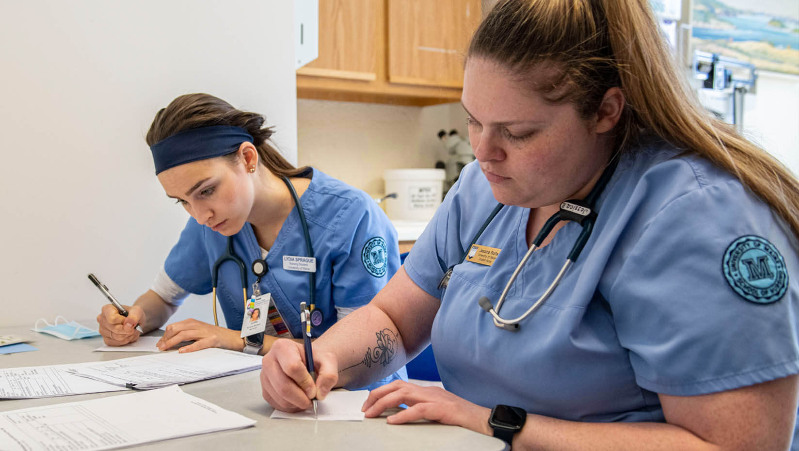 A photo of two nursing students completing paperwork at a table