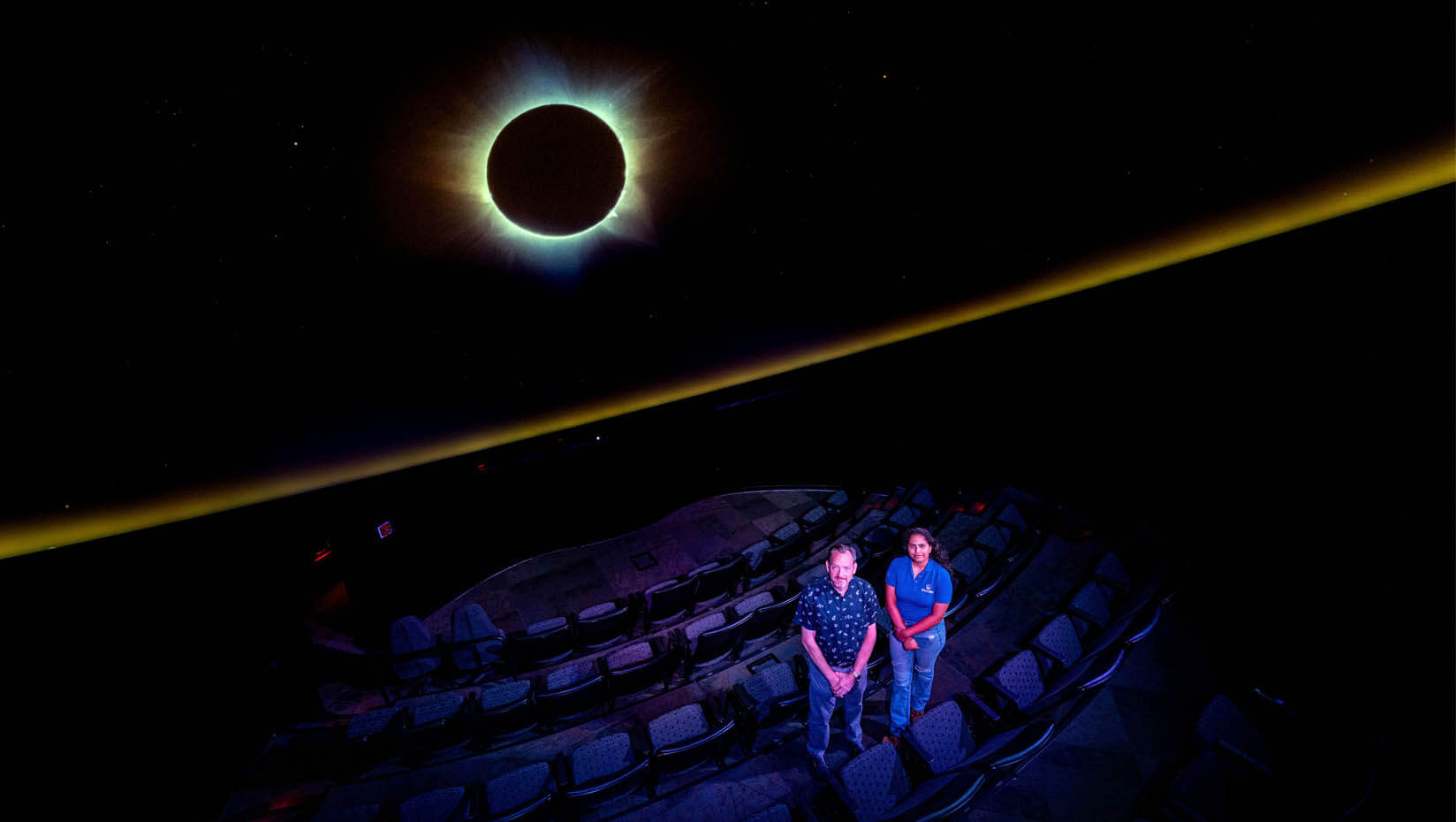 A photo of Shawn Laatsch and Nikita Saini in front a solar eclipse projection in the Versant Power Astronomy Center
