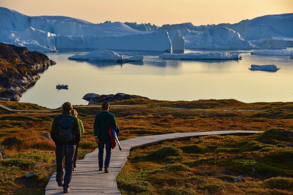 A photo of three people walking toward an iceberg