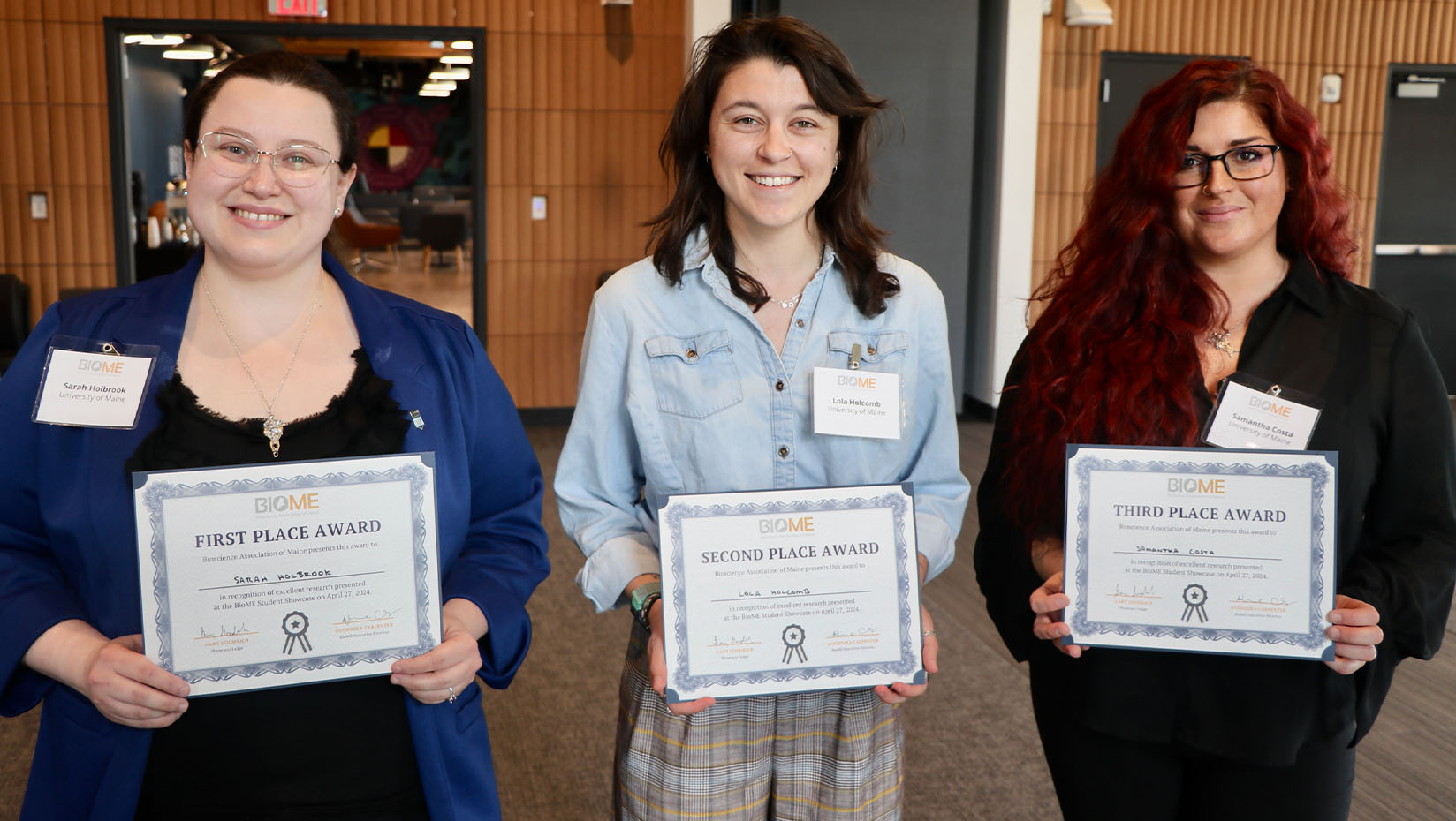 Photo of three people posing for a picture, smiling and holding certificates.