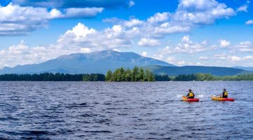 A photo of two people kayaking on a lake in front of Mount Katahdin