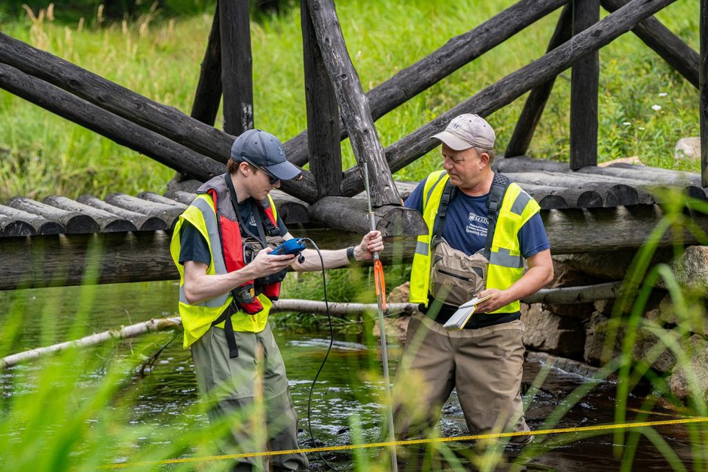 A photo of two people using a device to collect data in a stream