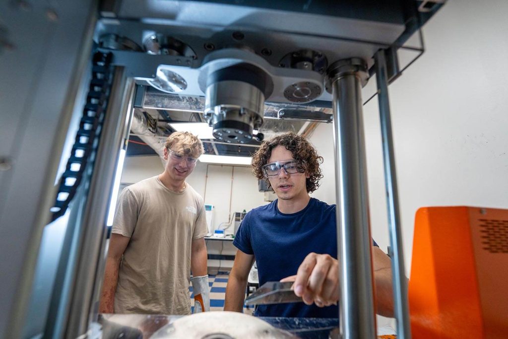 A photo of two people working with a machine in an engineering lab