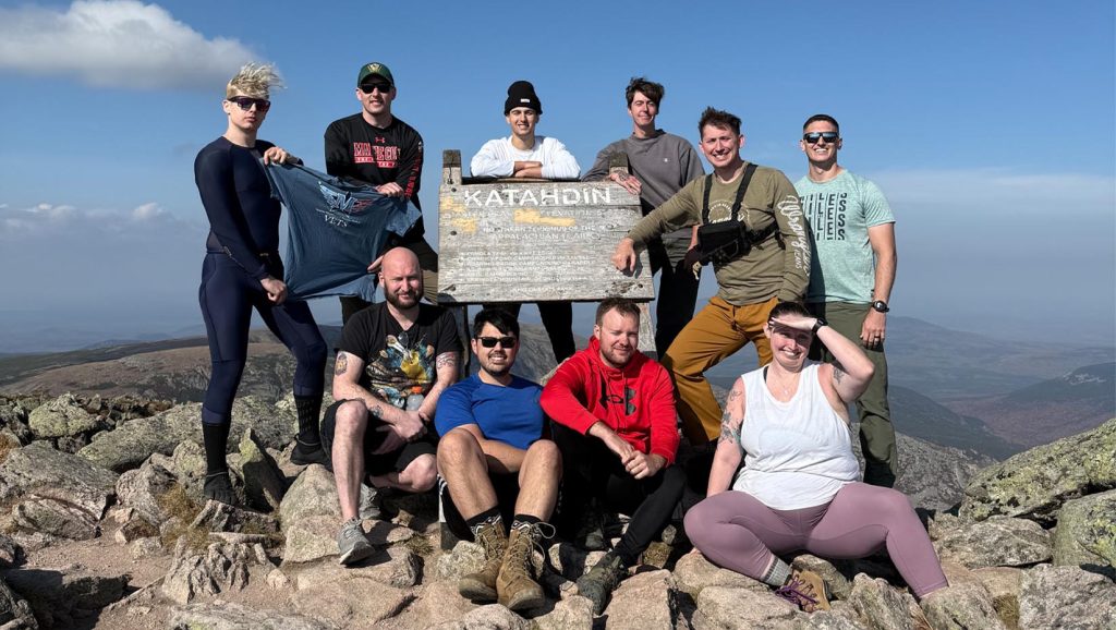 A photo of a group of people standing and sitting on a mountain top.