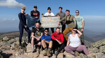 A photo of a group of people standing and sitting on a mountain top.