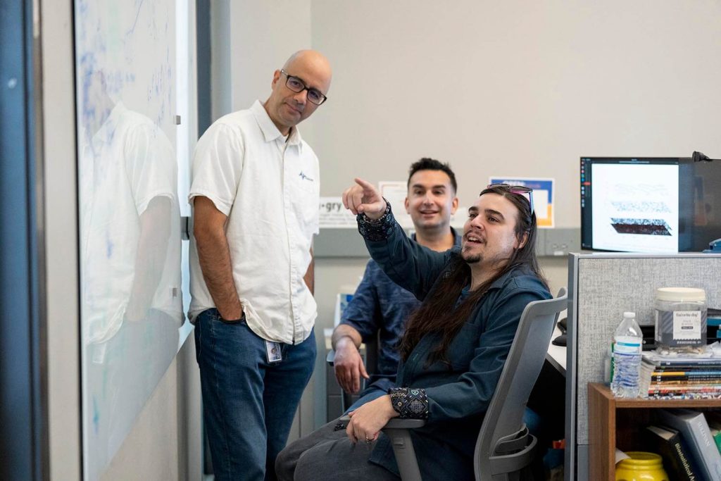 A photo of three people in front of a white board