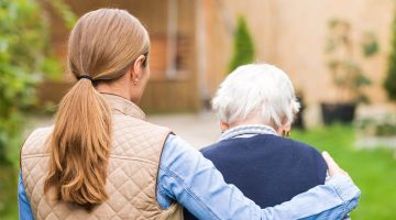A photo of two people walking outside. The person on the left has their arm wrapped around the person on the right.