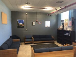 open room with concrete walls, 4 couches in square shape with a bookshelf to the left
