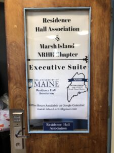 wood door with a sign behind a glass window that says 'Residence Hall Association & Marsh Island NRHH Chapter Executive Suite' 