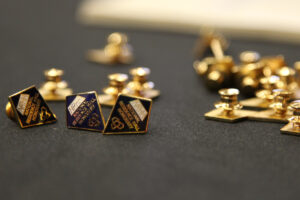 diamond shaped pins, dark blue and gold, writing that says 'NRHH National Residence Hall Honorary' 