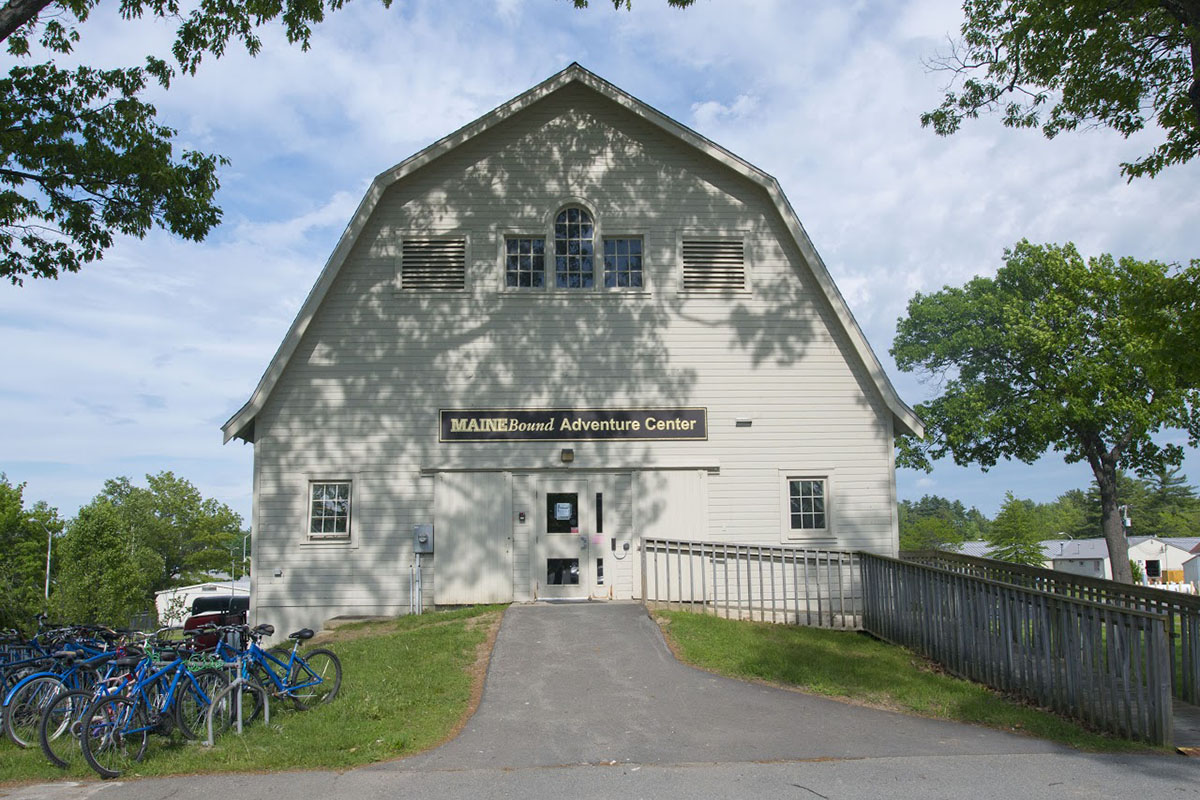 Maine Bound Adventure Center's white barn in front of a blue sky with white clouds